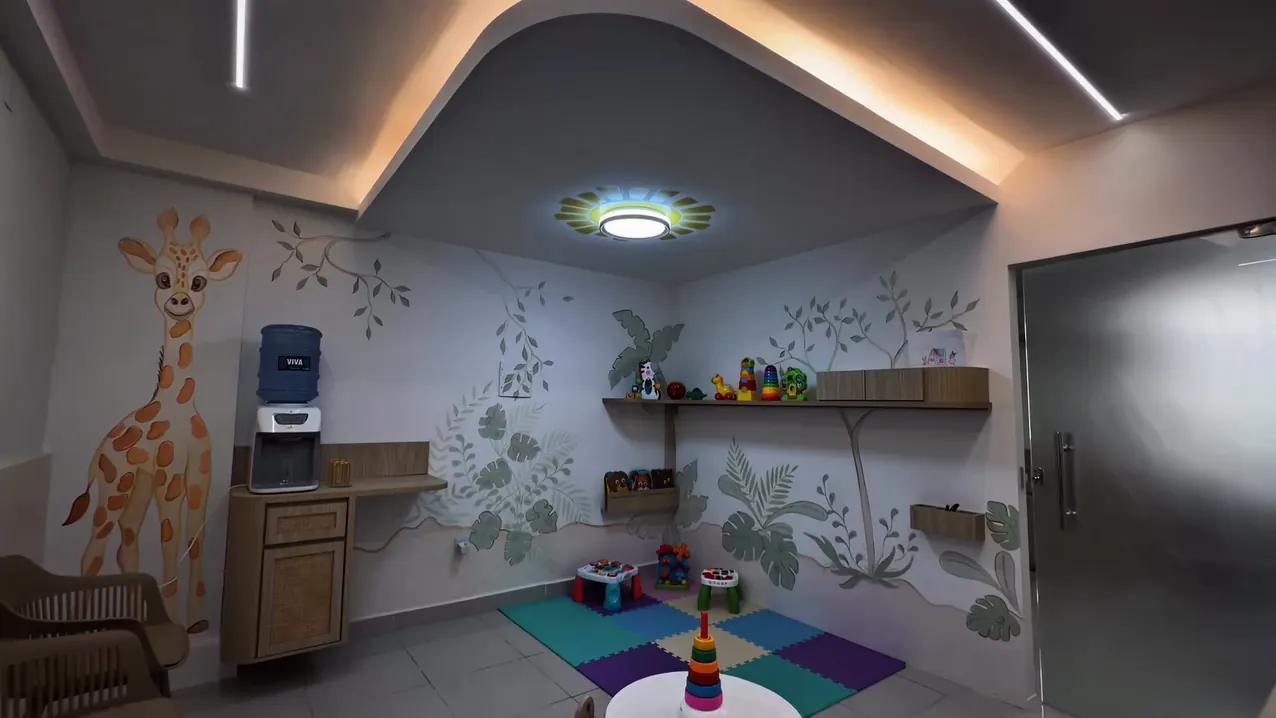 Recepção do consultório com espaço kids, tapete colorido e pintura de girafa na parede